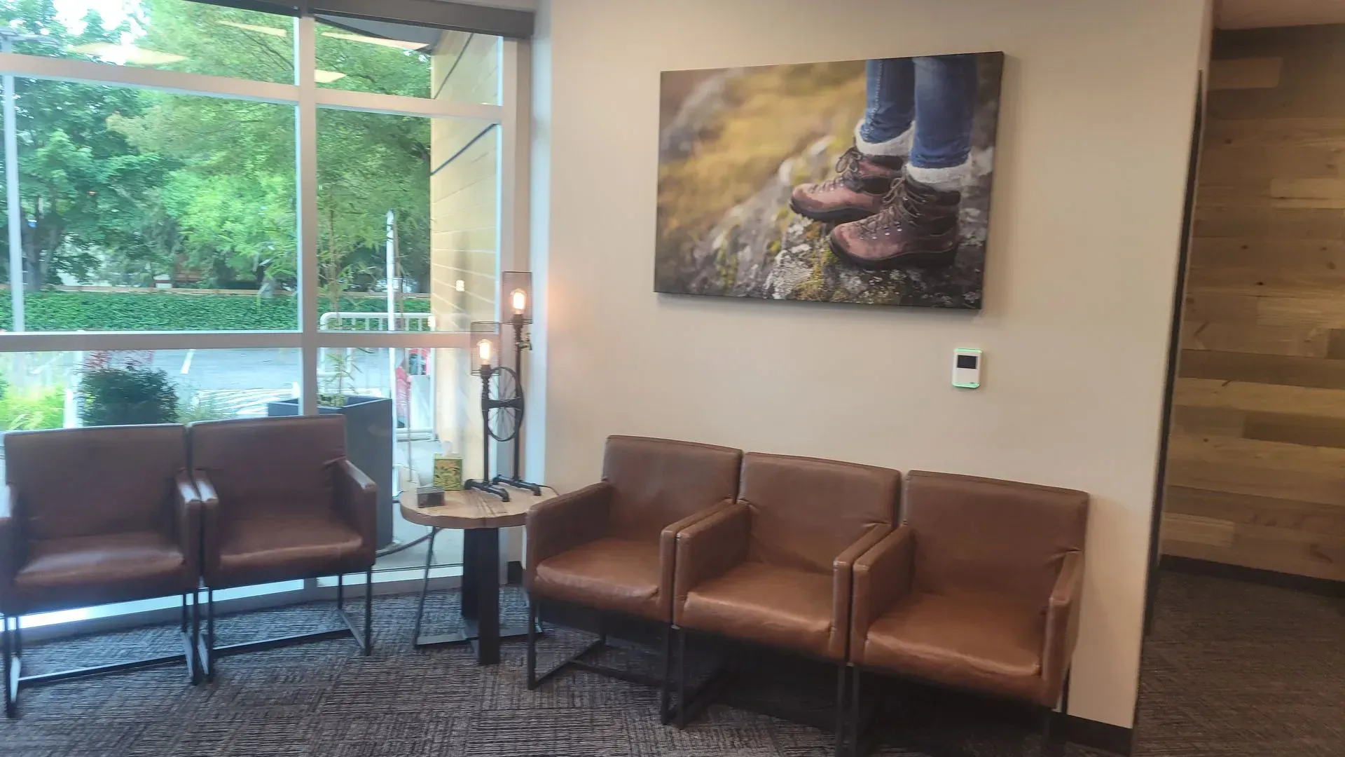 Waiting room with brown leather chairs, a small table, large window, and a nature-themed picture on the wall.