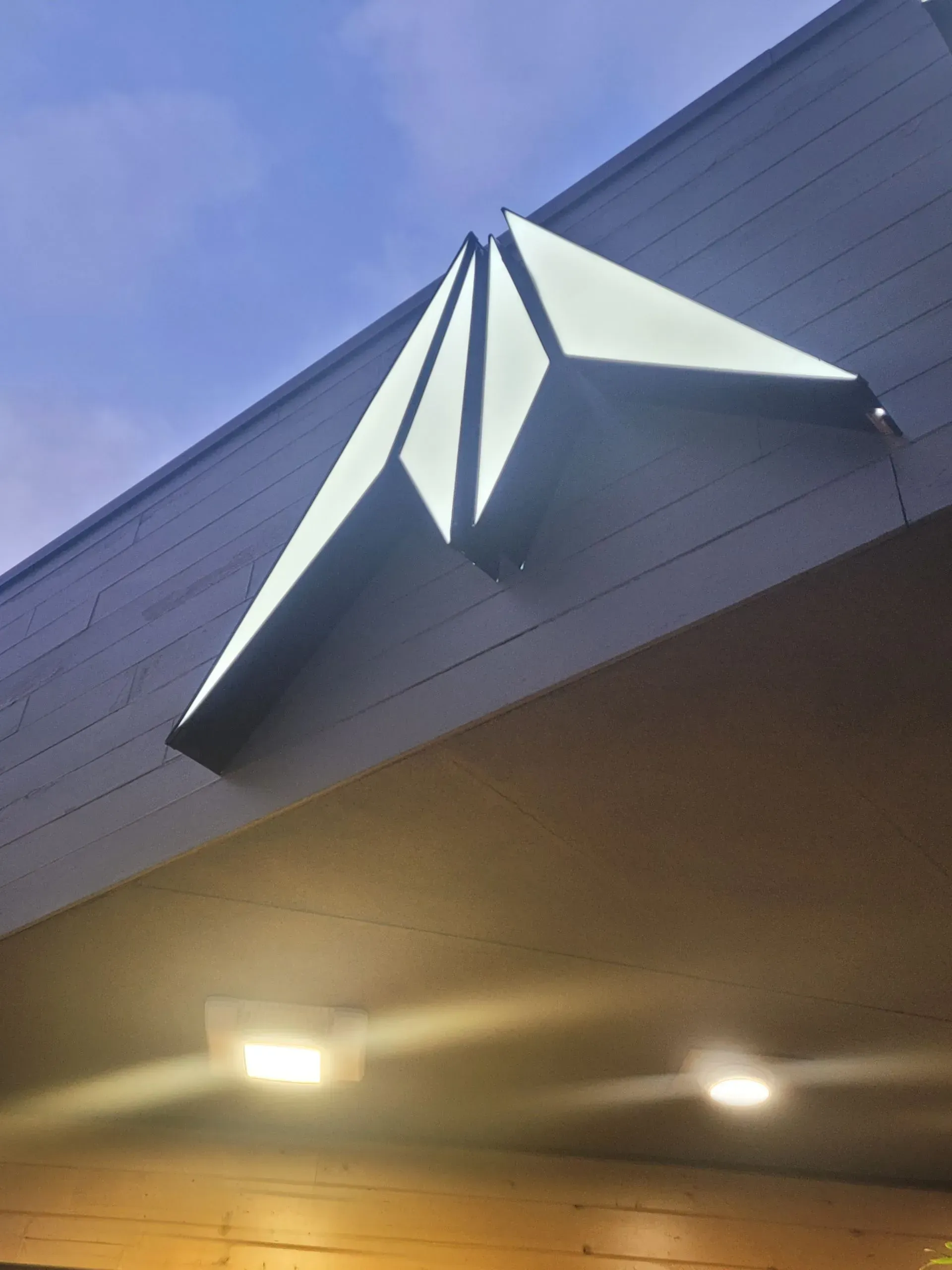 Geometric, illuminated sign on building exterior. Angular, white with dark outlines. Over a doorway.