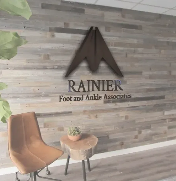 Lobby of Rainier Foot and Ankle Associates, wood paneled wall, logo, chair, tree stump table, small plant.