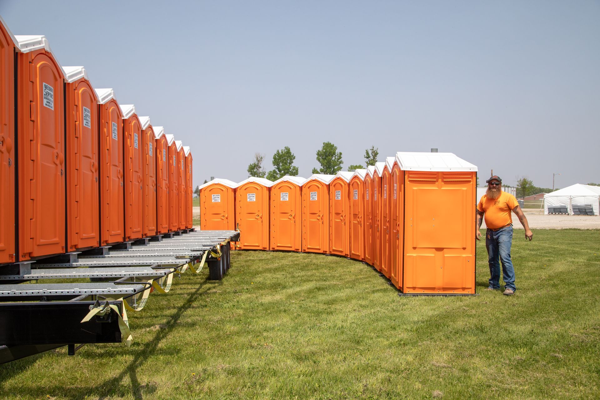 A man is standing in front of a row of orange portable toilets