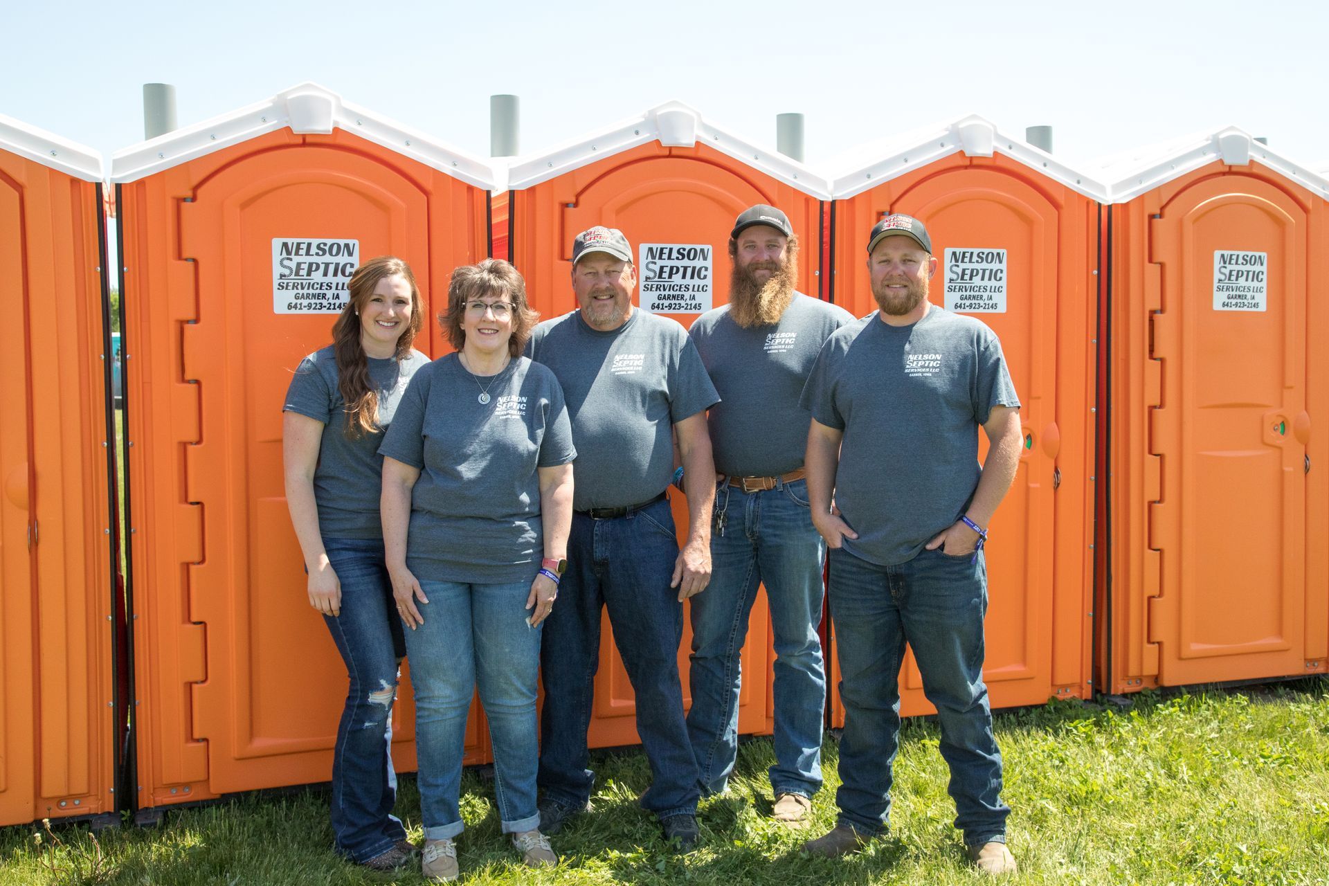 A group of people are posing for a picture in front of portable toilets