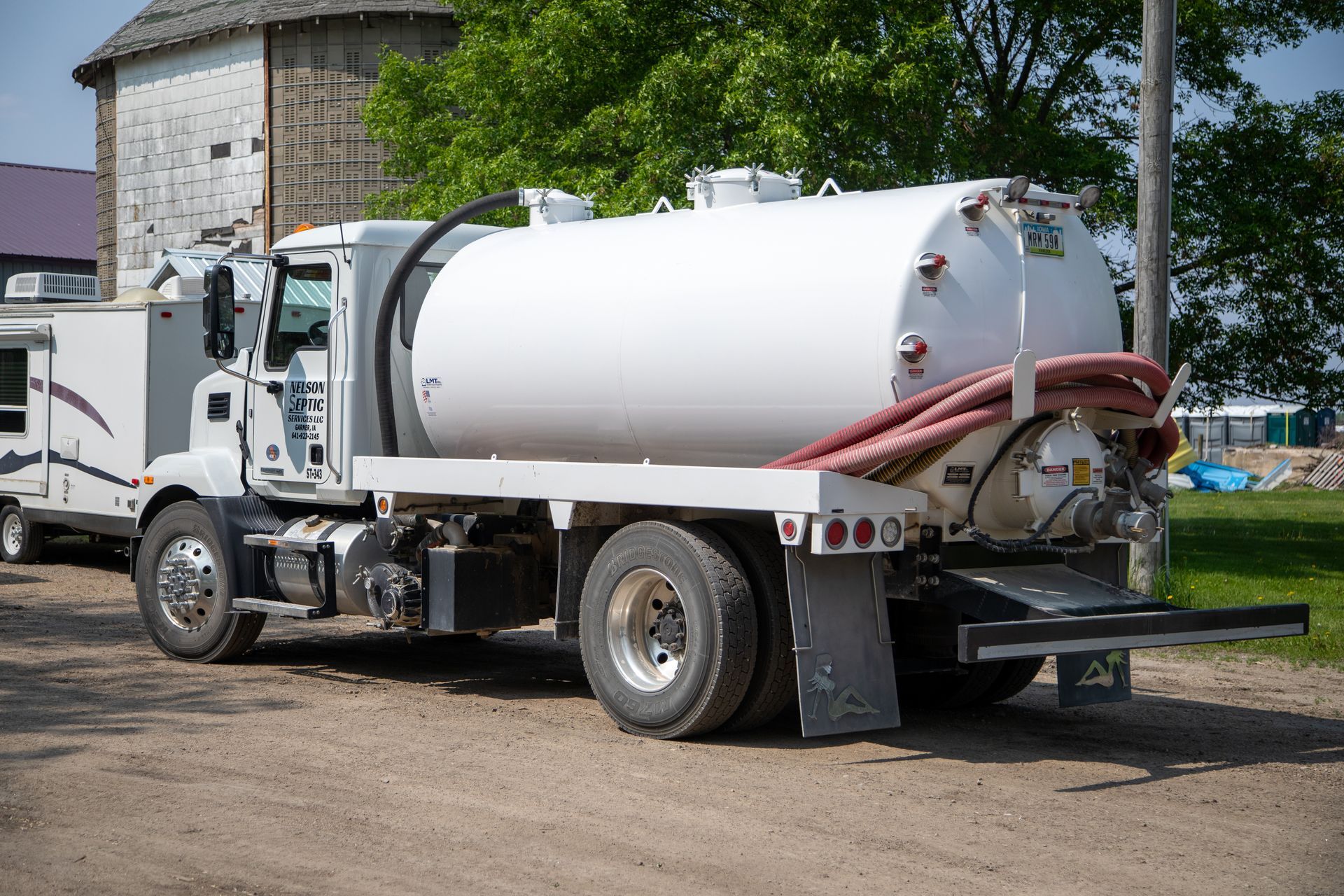 A white vacuum truck is parked in a dirt lot