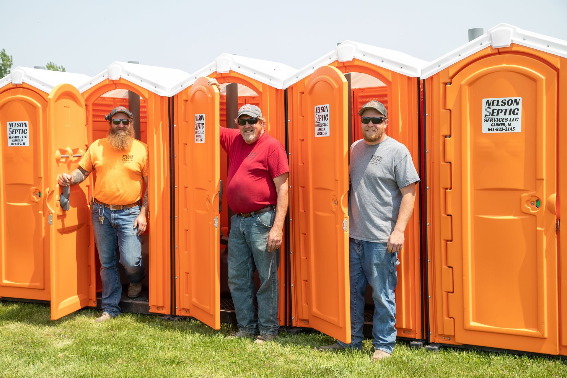 Three men are standing in front of a row of orange portable toilets