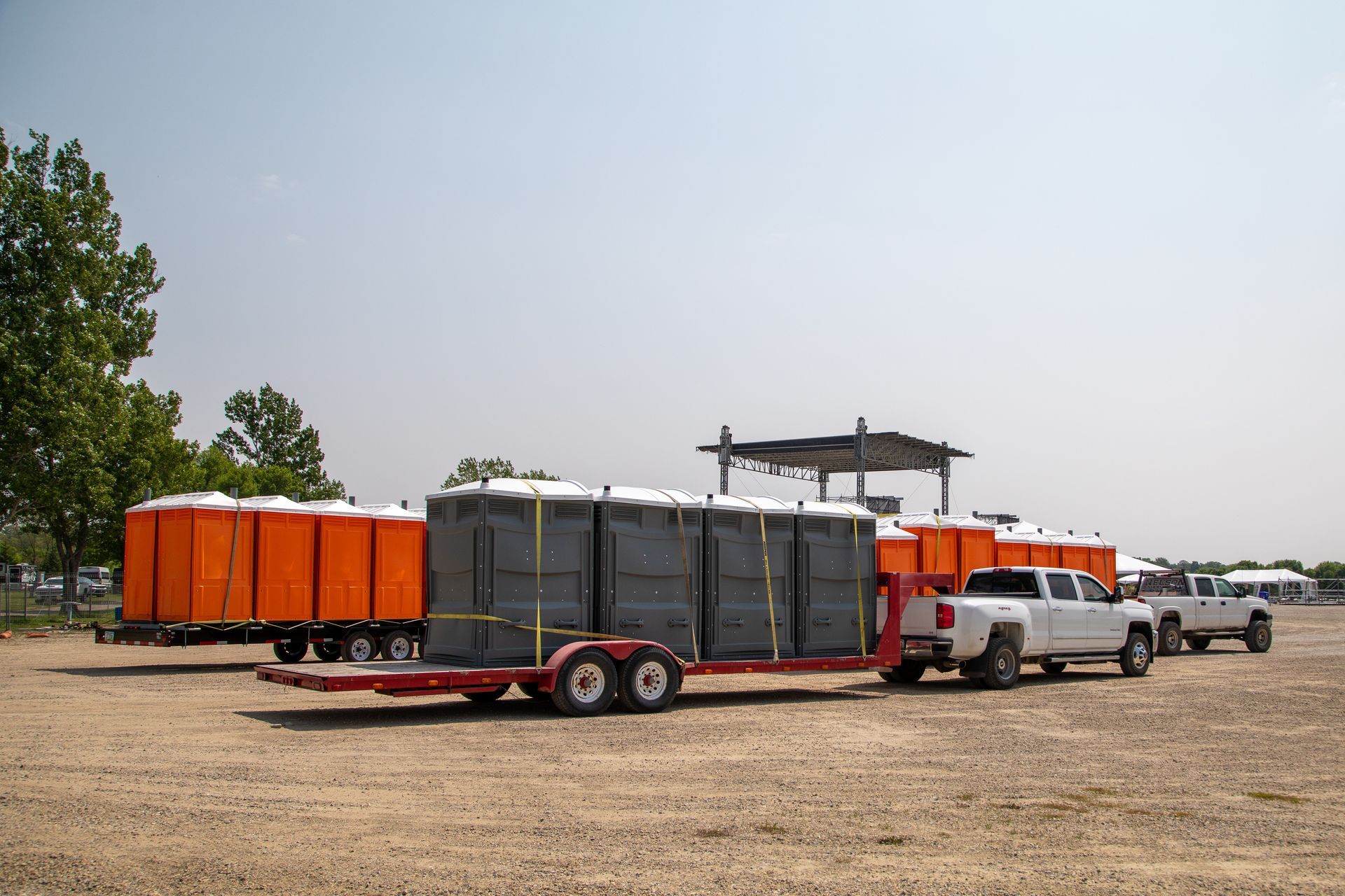 A white truck is pulling a trailer full of portable toilets