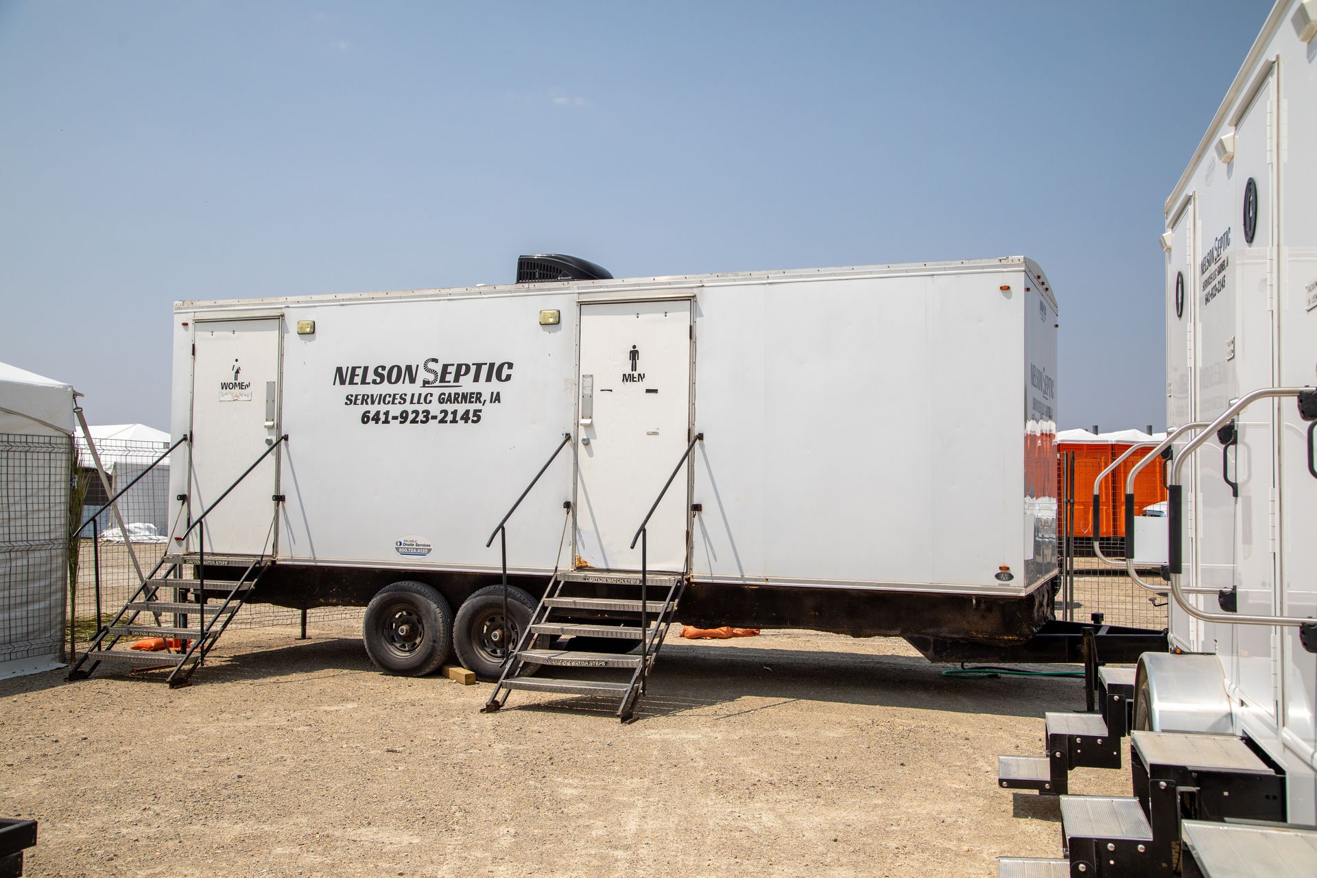 A white trailer with stairs attached to it is parked in a dirt field