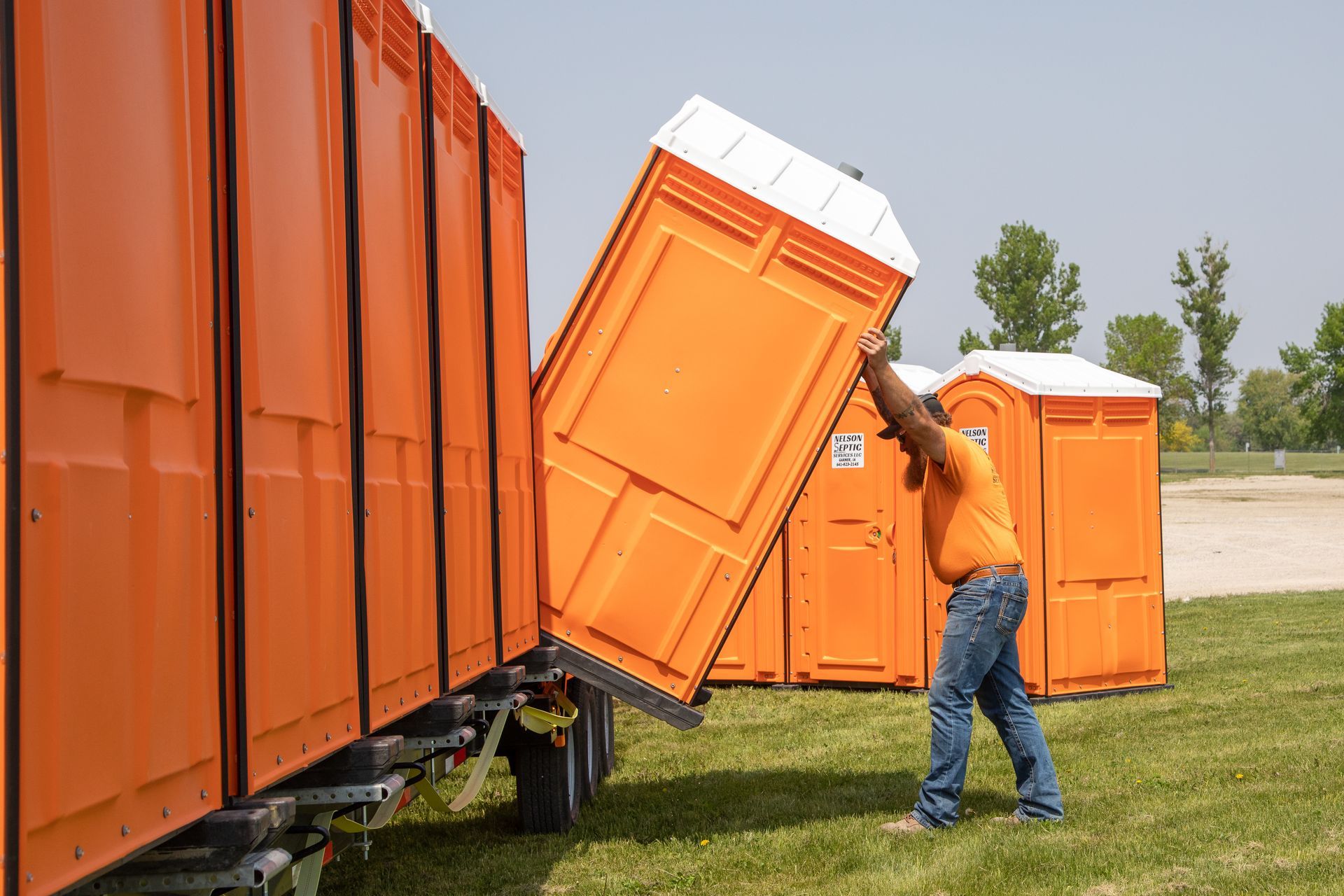 A man is lifting a portable toilet out of a trailer
