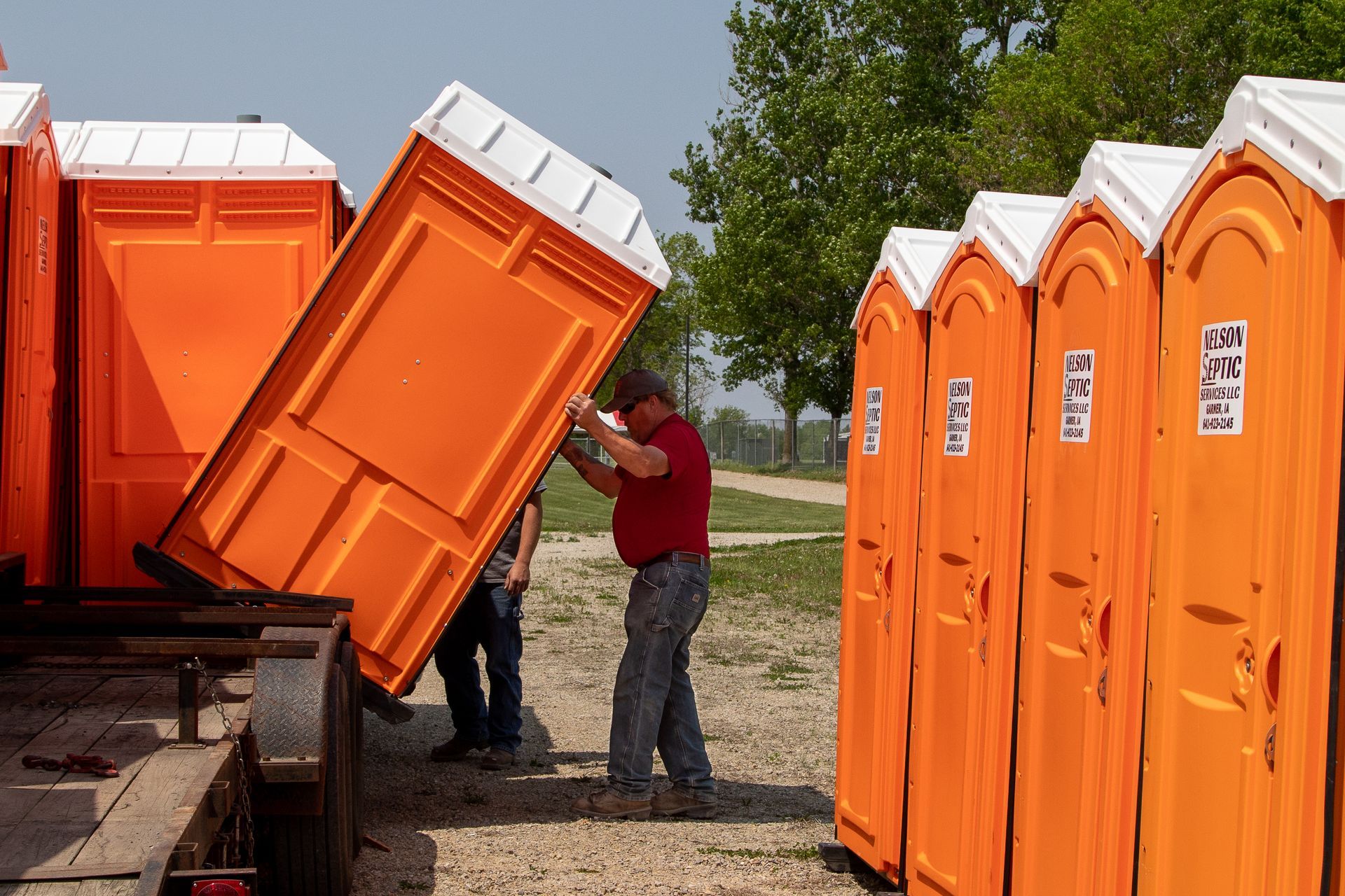A man is standing next to a row of orange portable toilets