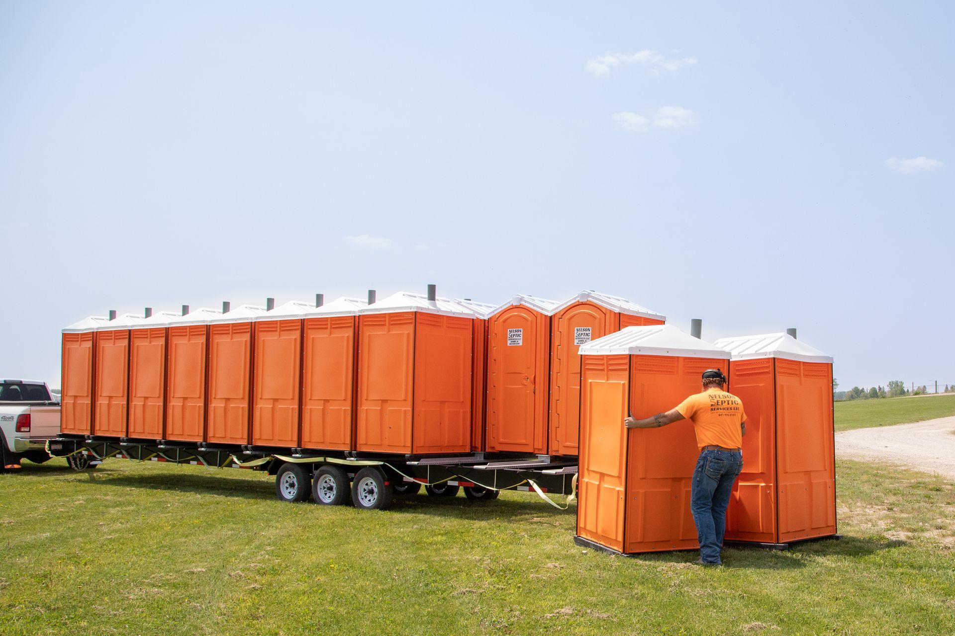 A man is standing next to a trailer filled with orange portable toilets