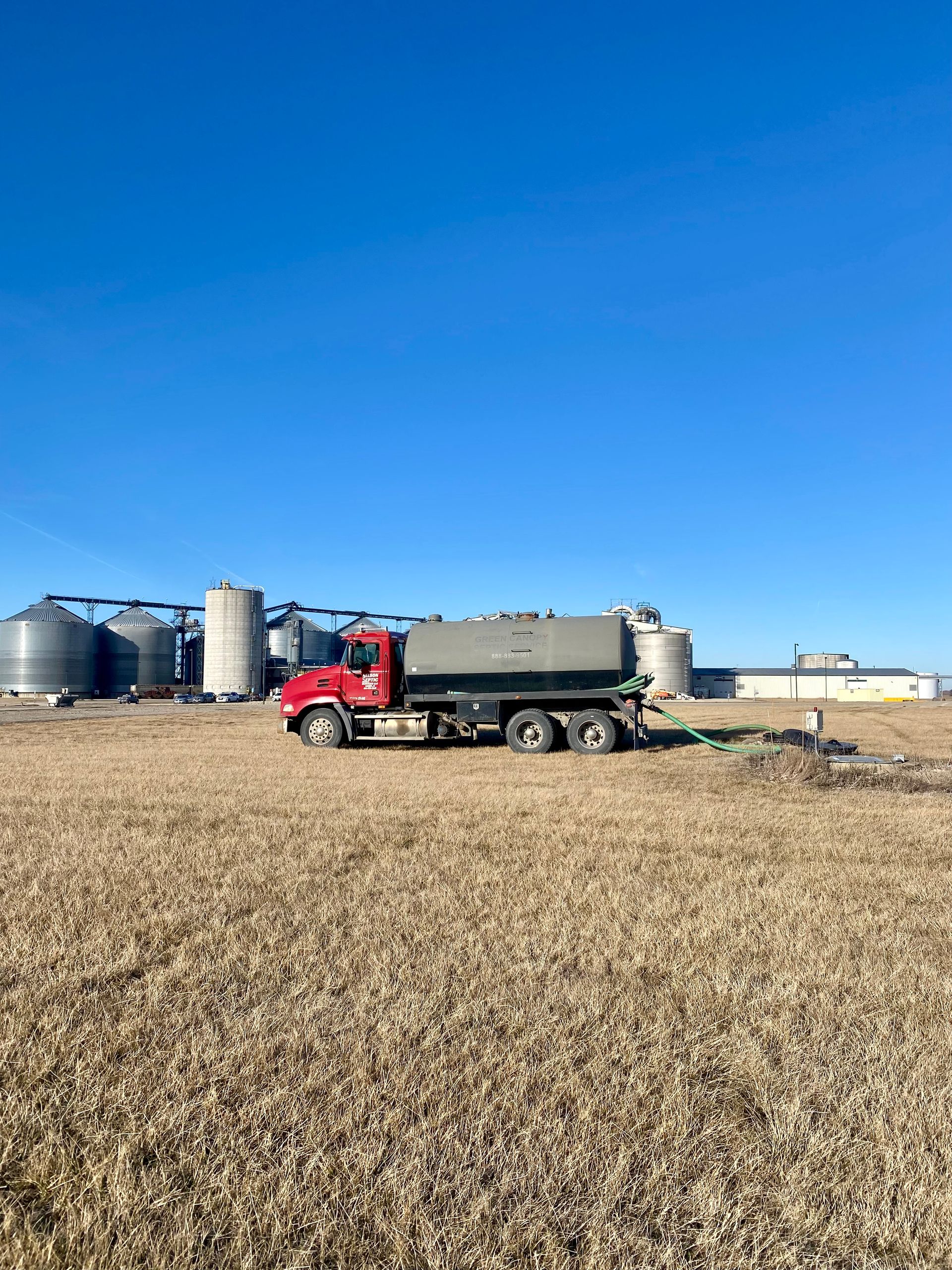 A red truck is parked in a field with silos in the background