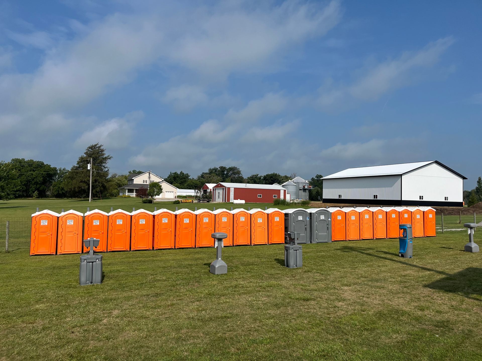 A row of orange portable toilets are lined up in a grassy field
