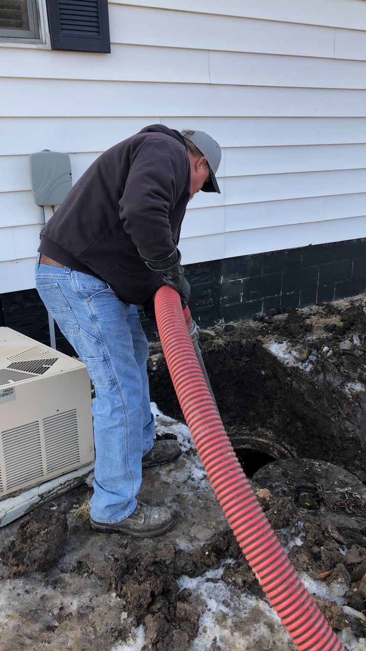A man is using a red hose to pump dirt into a hole in the ground