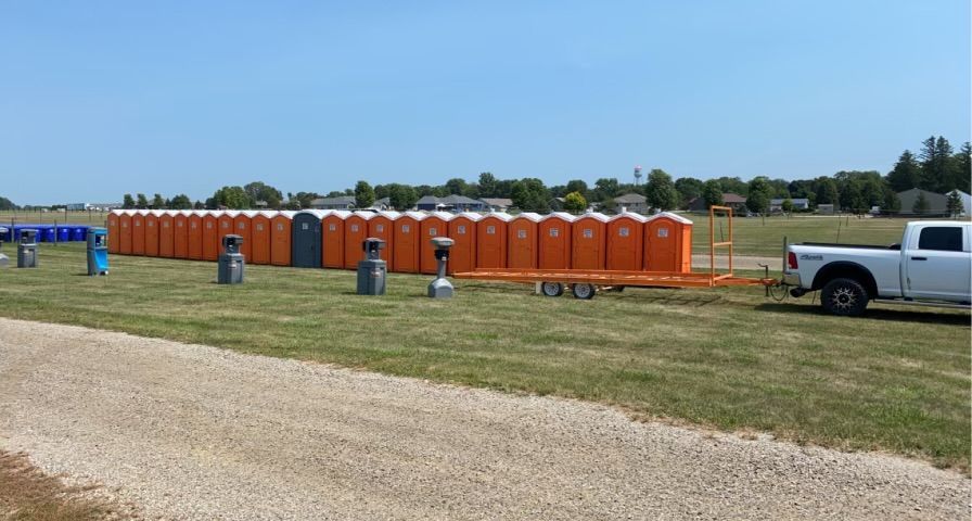 A white truck is pulling a trailer full of portable toilets