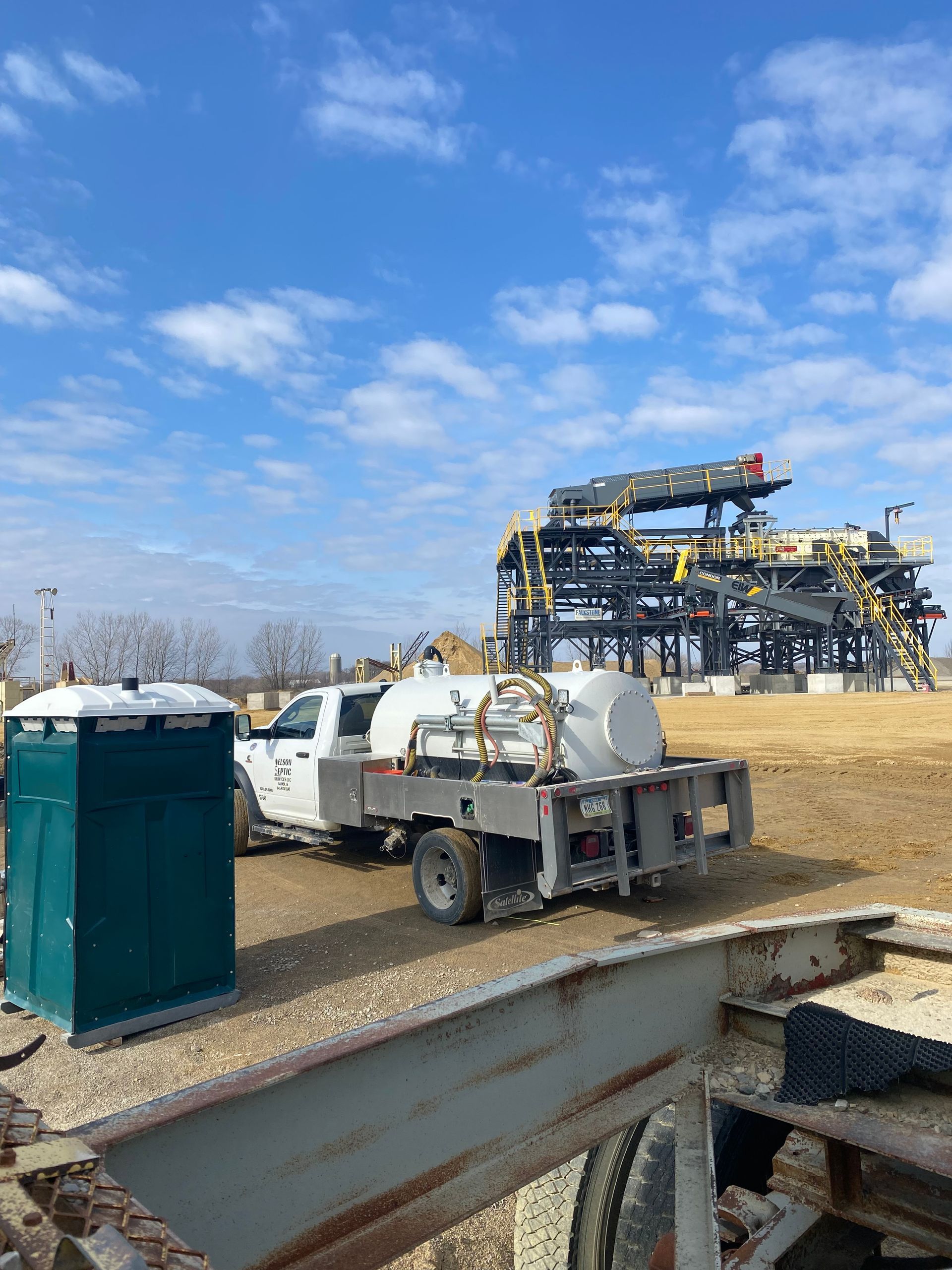 A white truck is parked in a field next to a green portable toilet