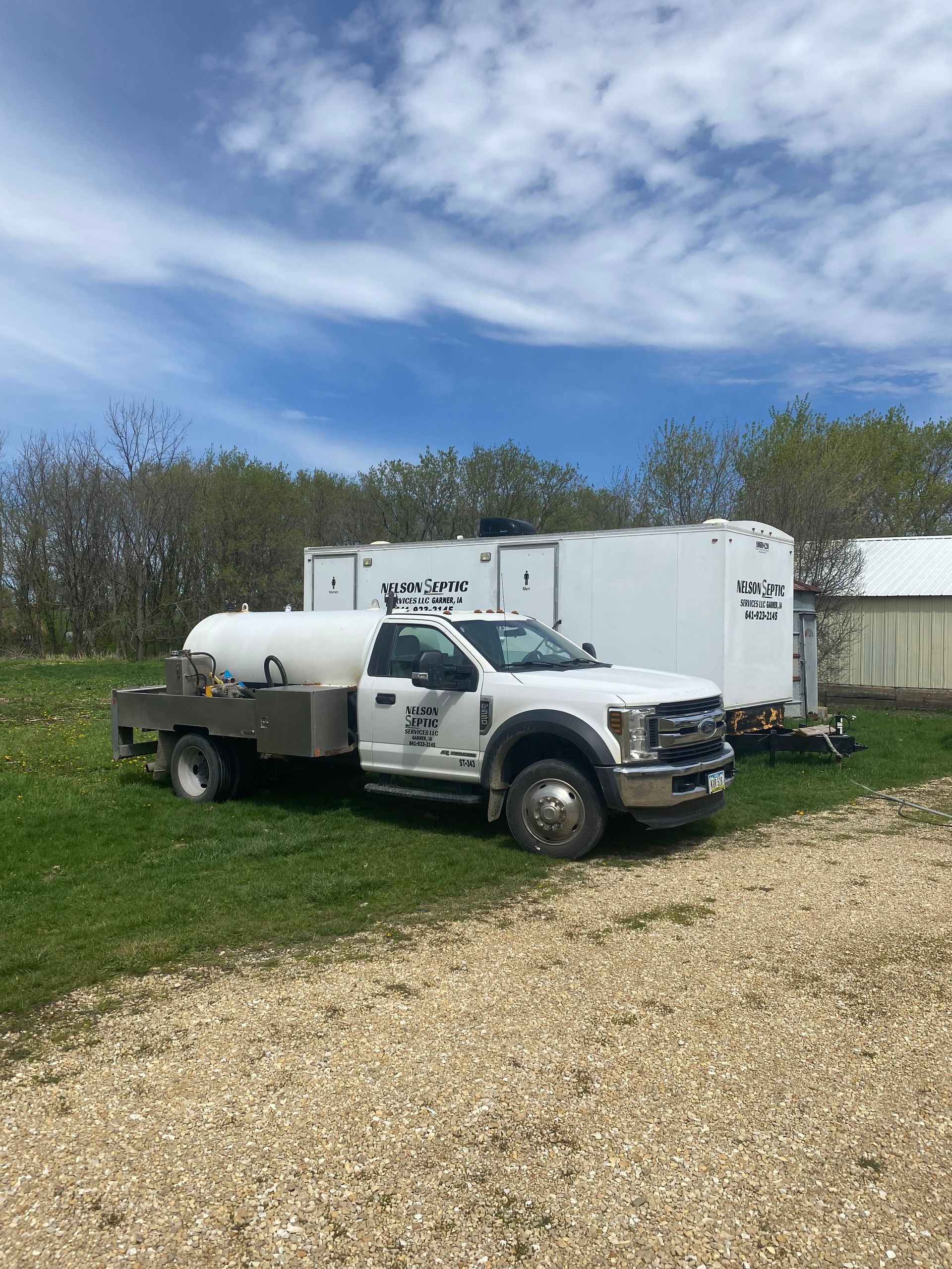 A white truck with a tank on the back is parked in a gravel lot