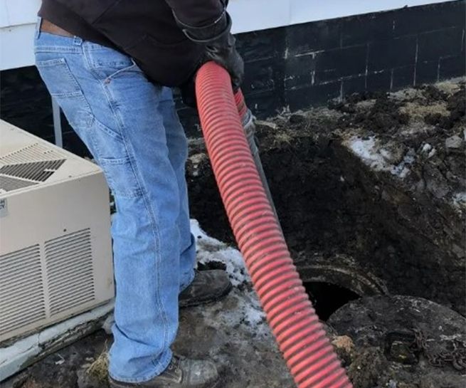 A man is pumping a red hose into a hole in the ground