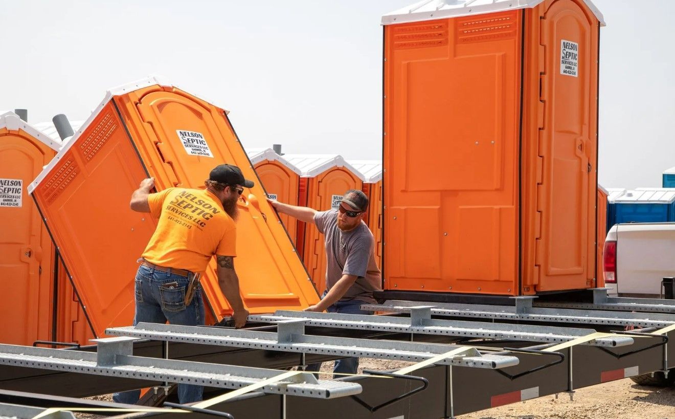Two men are working on a trailer with portable toilets in the background