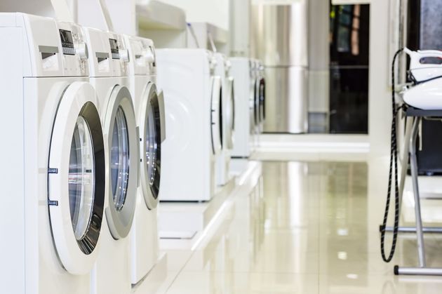 A row of white front-loading washing machines in a bright, clean laundry facility.