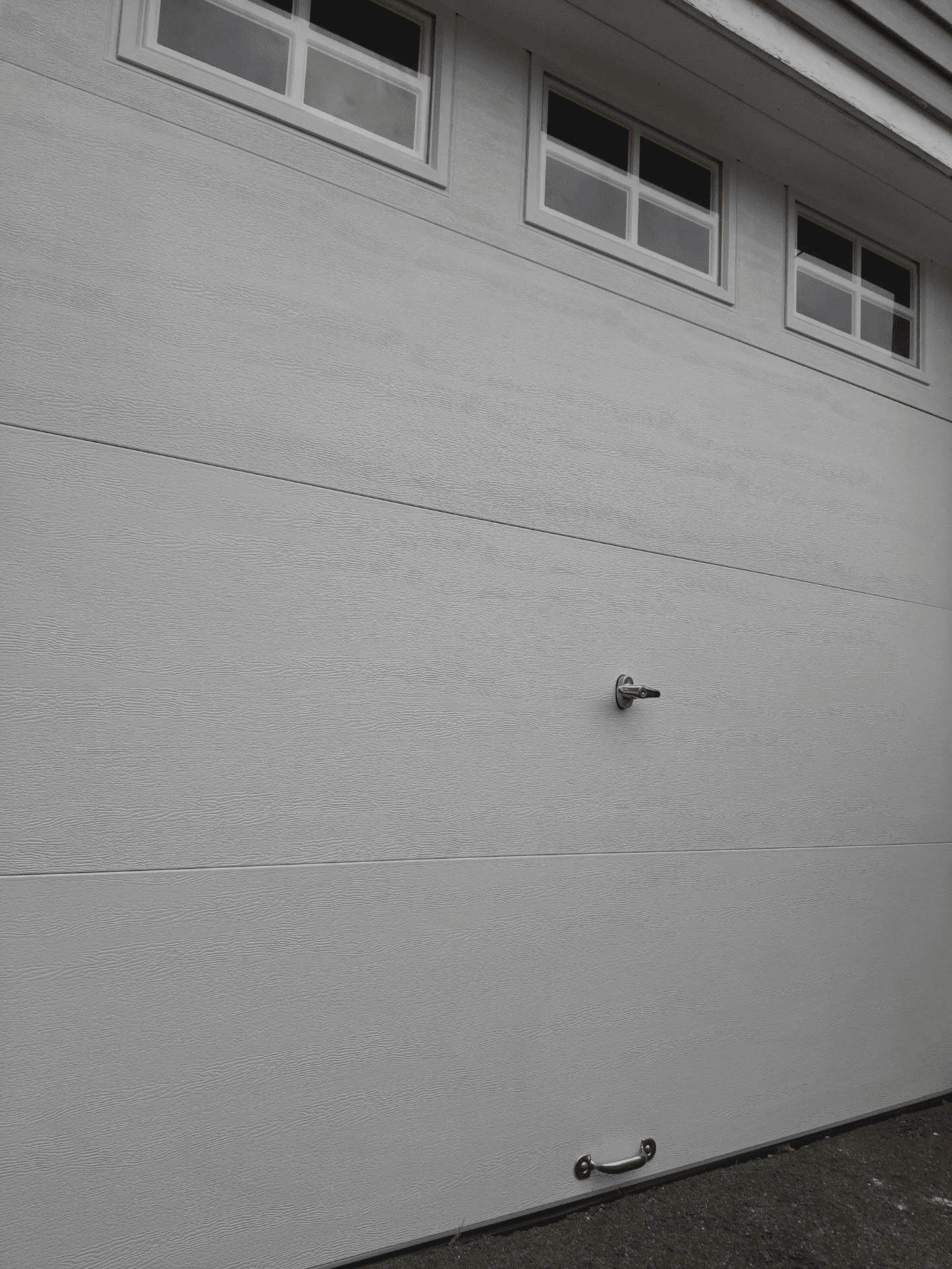 A black and white photo of a garage door with a handle and windows.