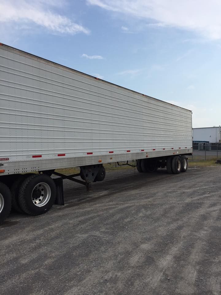 White semi-trailer parked on a paved lot under a blue sky.