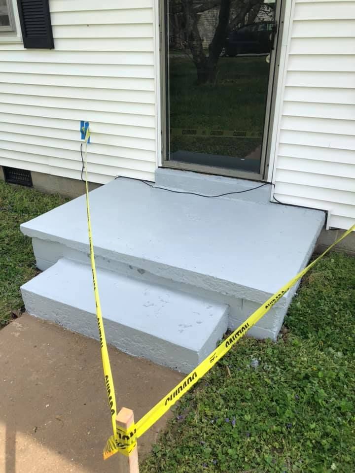 Freshly painted gray porch steps and landing blocked off with yellow caution tape beside a house entrance