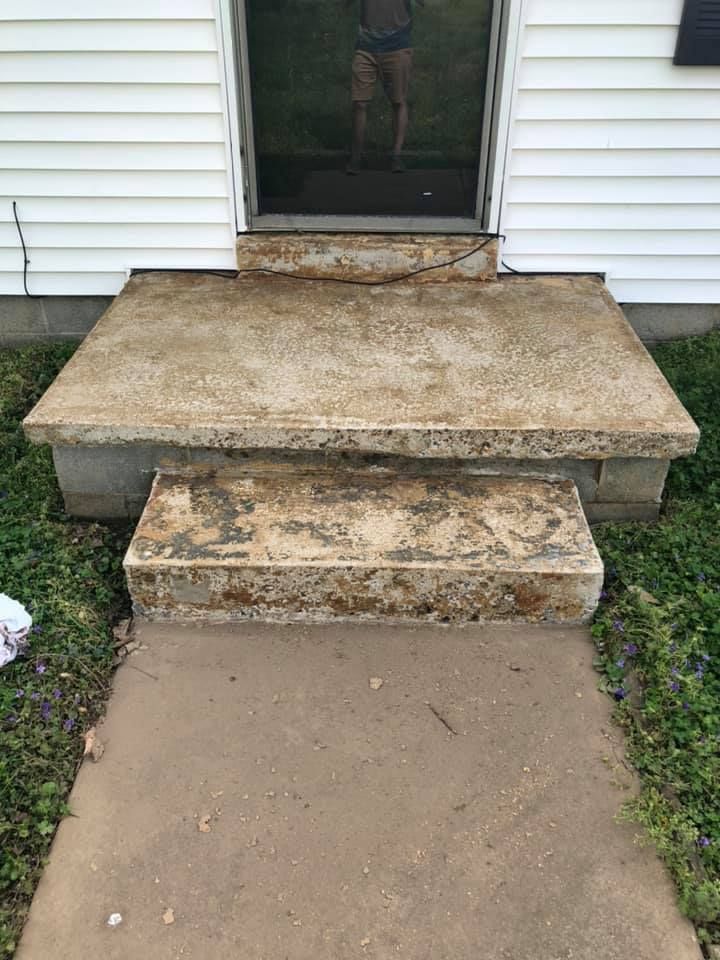Weathered concrete front steps leading to a doorway with white siding and a screen door