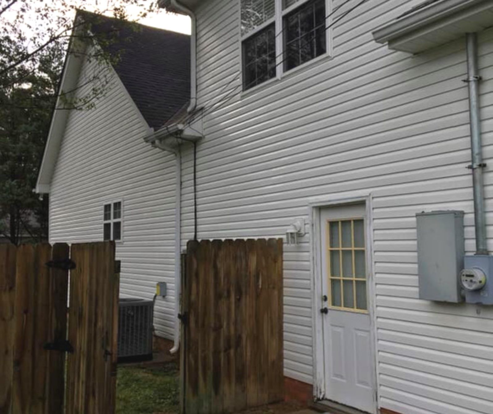 White house exterior with side door, wooden fence, and utility meters beside a narrow patio area