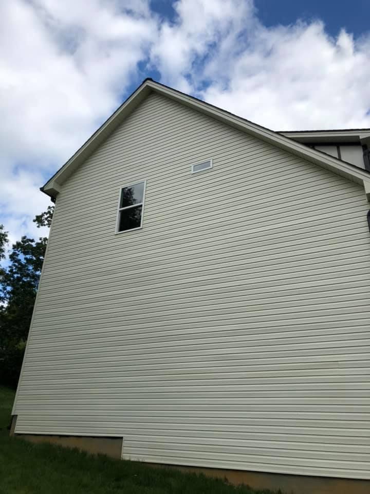 White vinyl-sided house exterior with a gabled roof and a small upper window against a cloudy sky