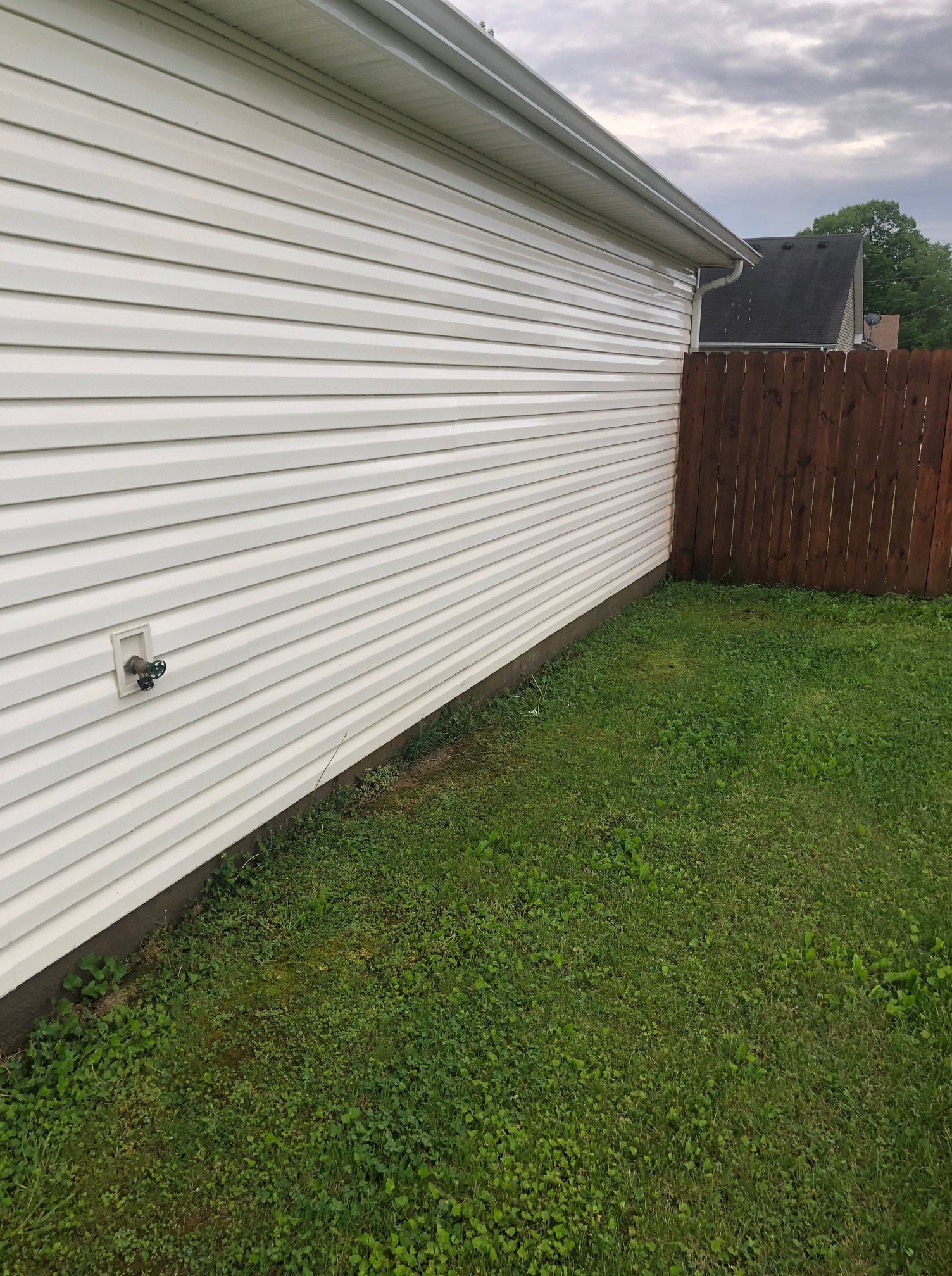White house siding beside a grassy yard and brown wooden fence under cloudy skies