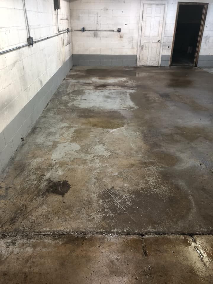 Empty industrial room with stained concrete floor and white tiled walls, showing wear and dirt.