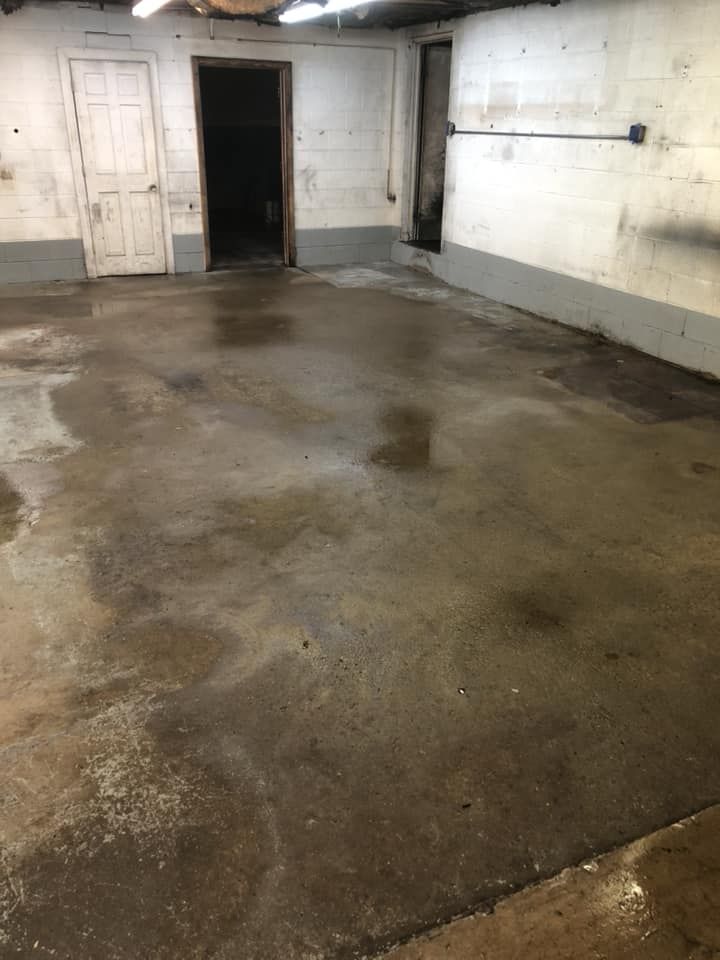 Empty concrete basement with wet floor, white walls, and an open doorway.
