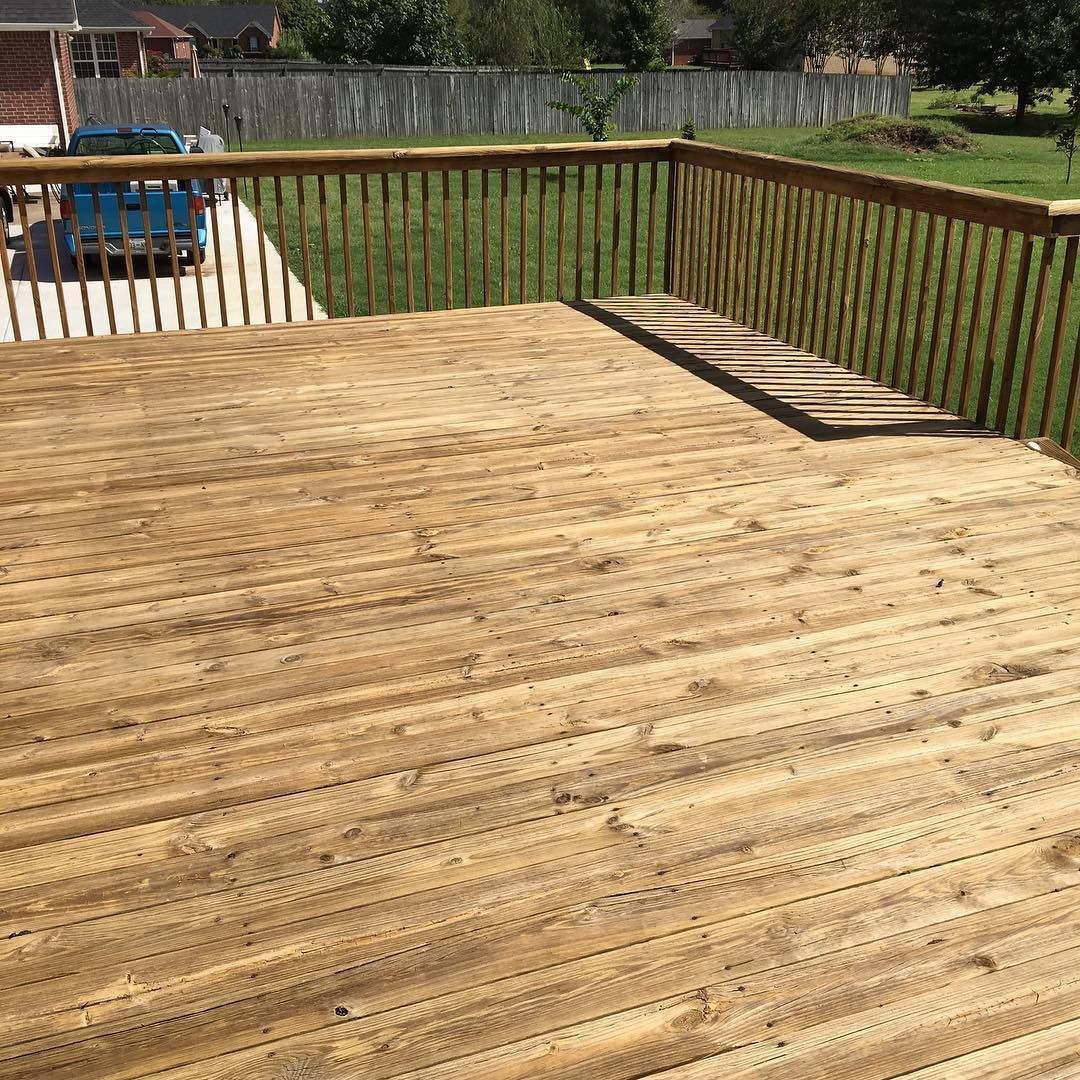 Wooden deck with railing overlooking a grassy yard and a small blue play structure in the background