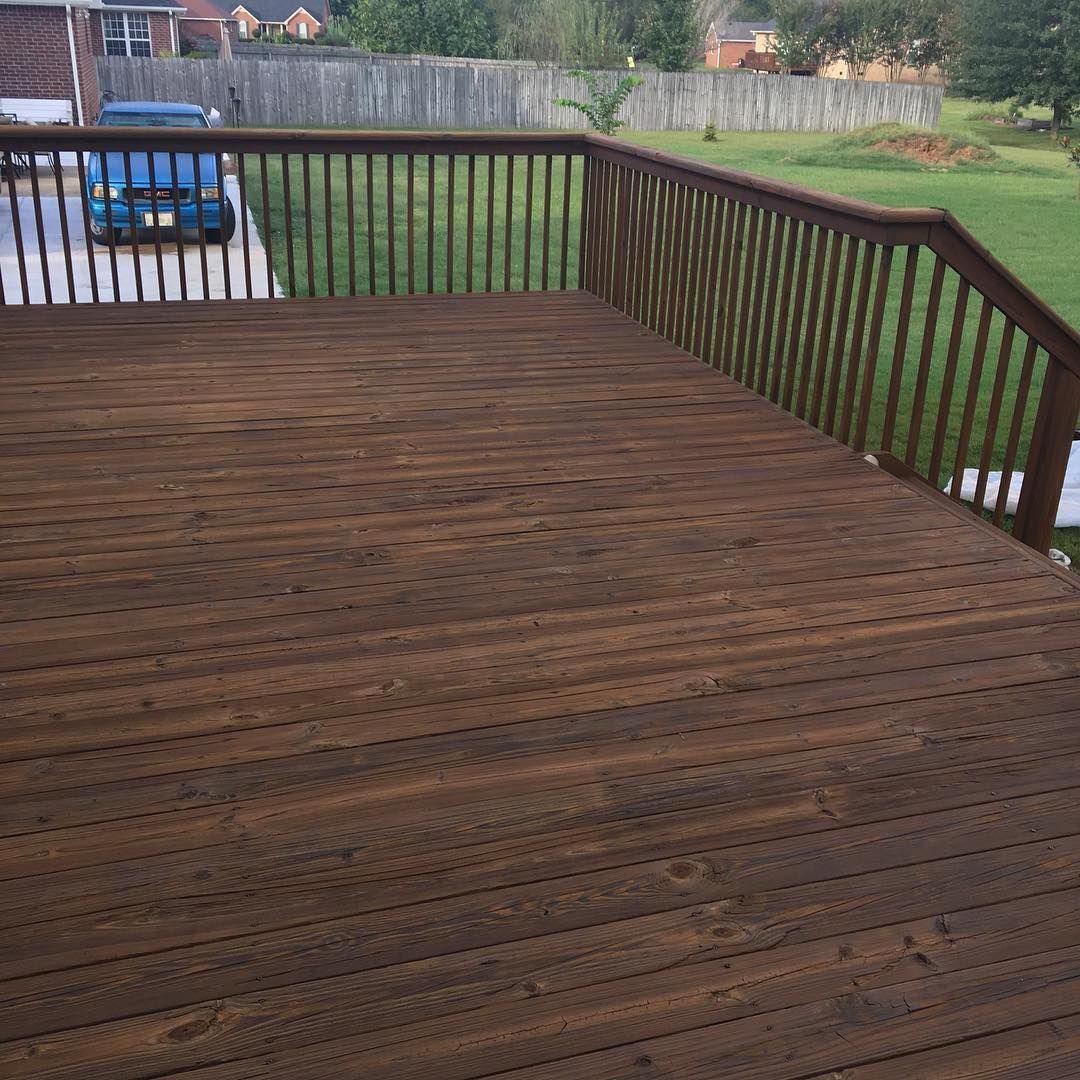 Wooden deck with dark railings overlooking a grassy yard, with a blue car visible in the background.