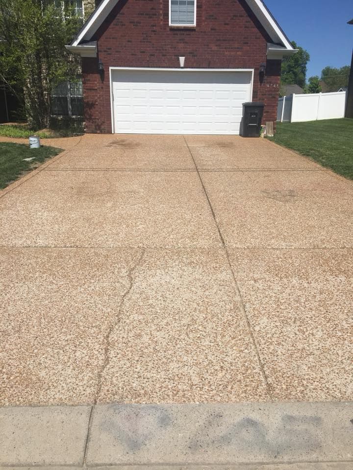 Concrete driveway leading to a white garage on a brick house under a sunny sky