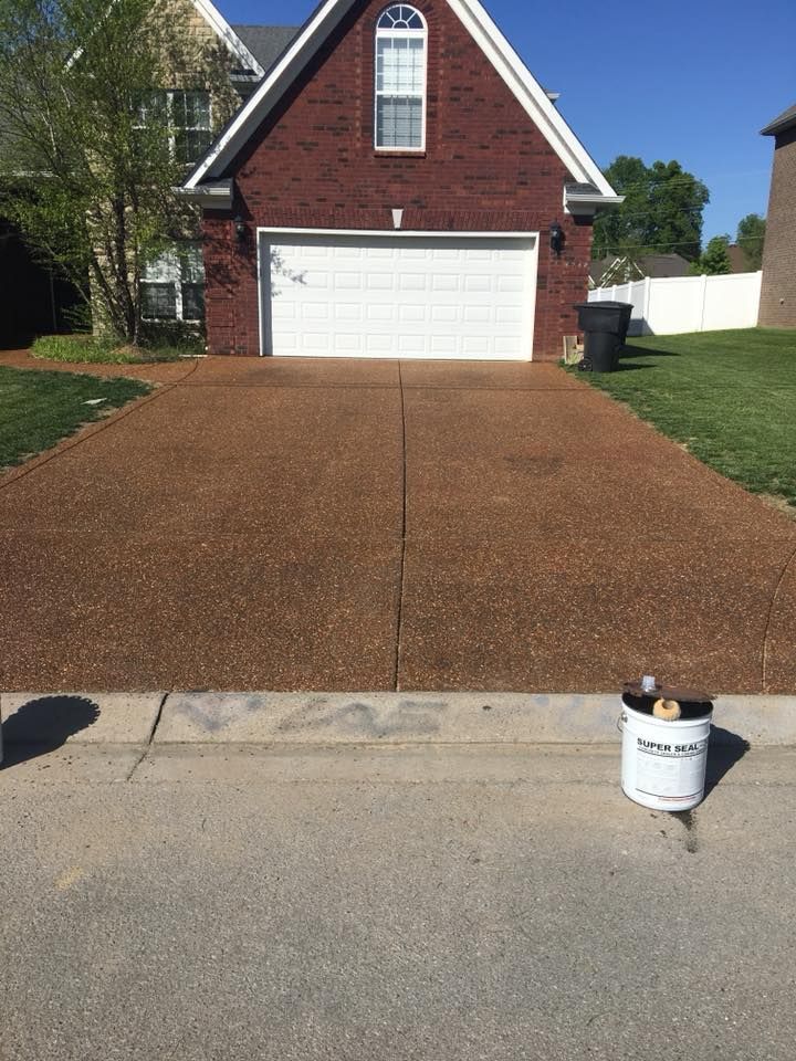Brick house with white garage and newly resurfaced brown driveway; small bucket on curb in foreground
