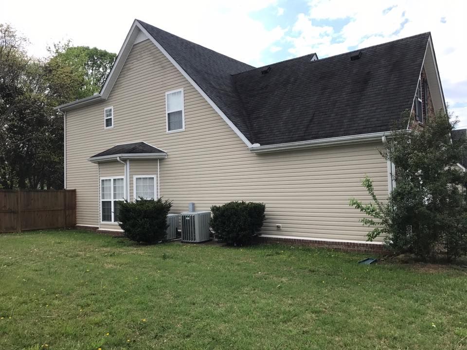 Suburban beige house with dark roof and small fenced backyard lawn