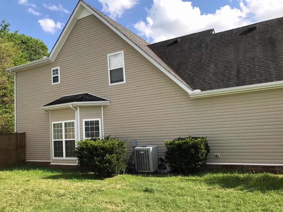 Back of beige house with white-trimmed windows, sliding glass door, shrubs, and a grassy yard.