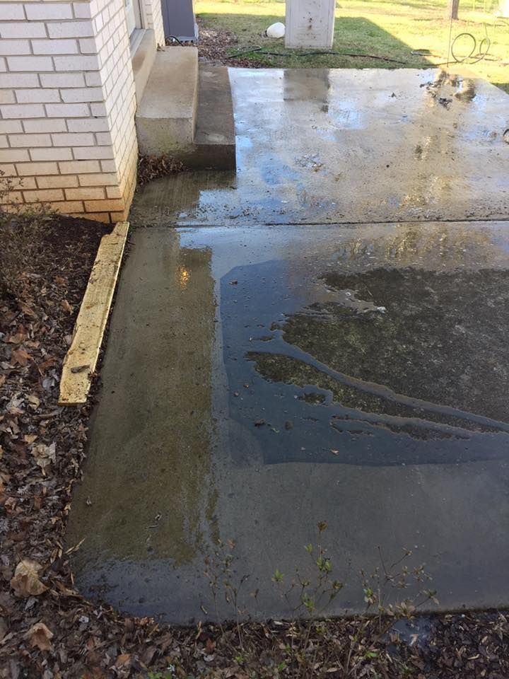 Icy wet sidewalk beside a brick building, with a small puddle and patchy ice.