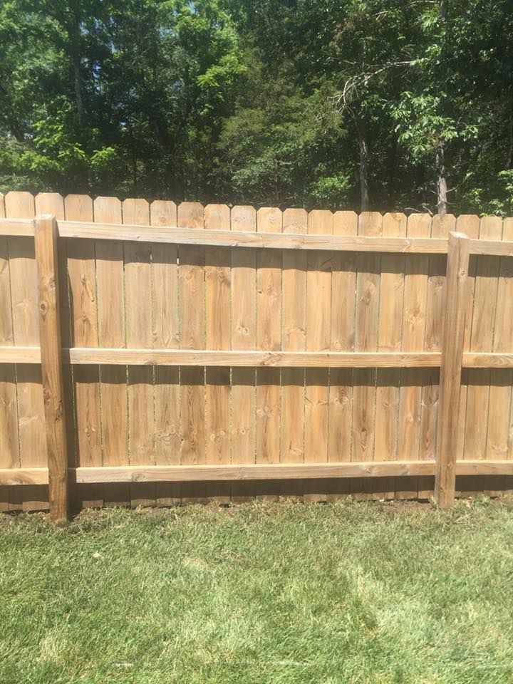 Wooden backyard fence with grass in front and trees behind
