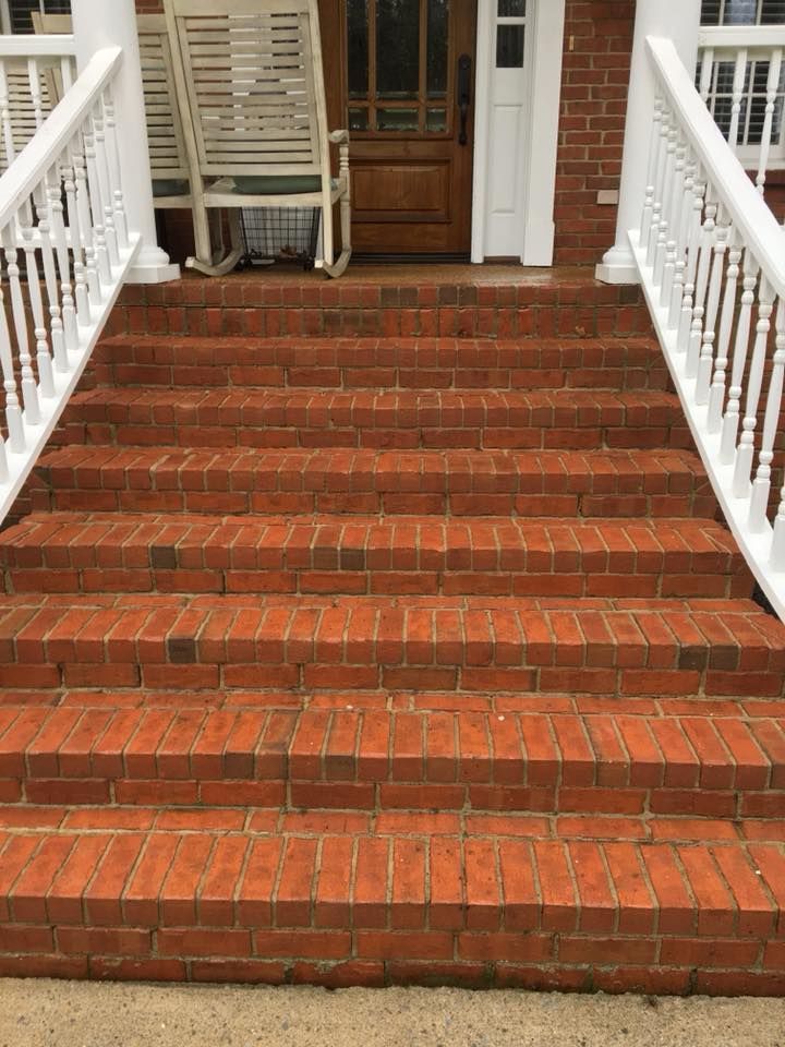 Brick front steps leading to a porch with white railings and a wooden door