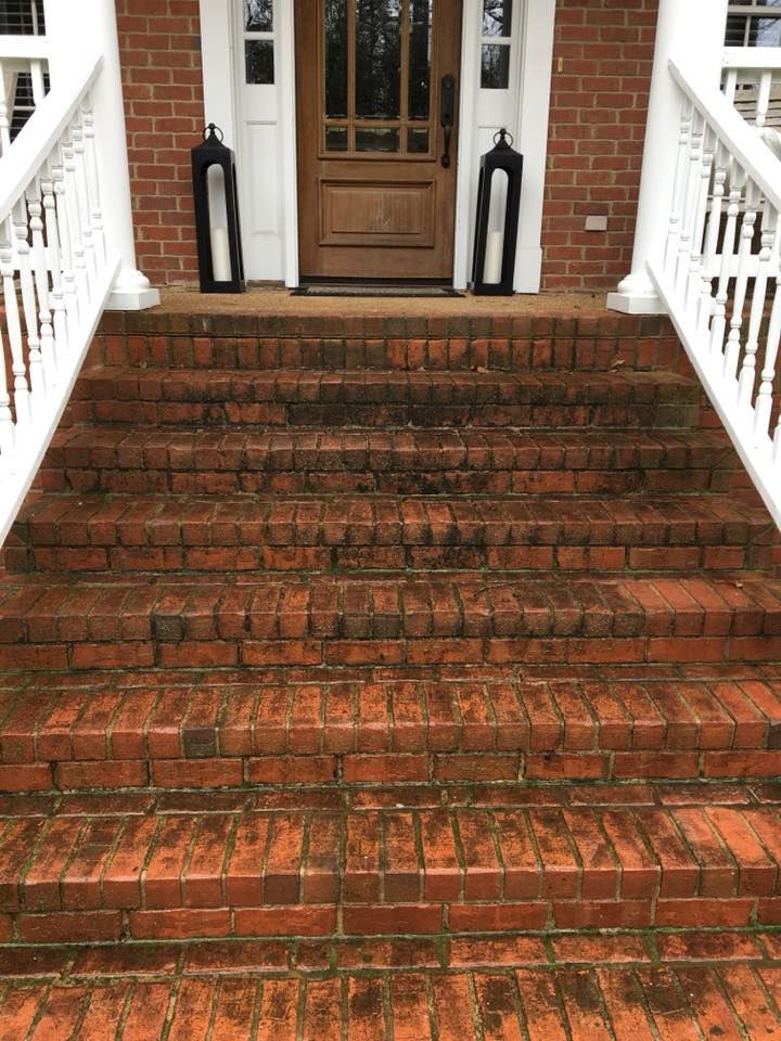 Brick front steps leading to a wooden door, flanked by white railings and black lanterns