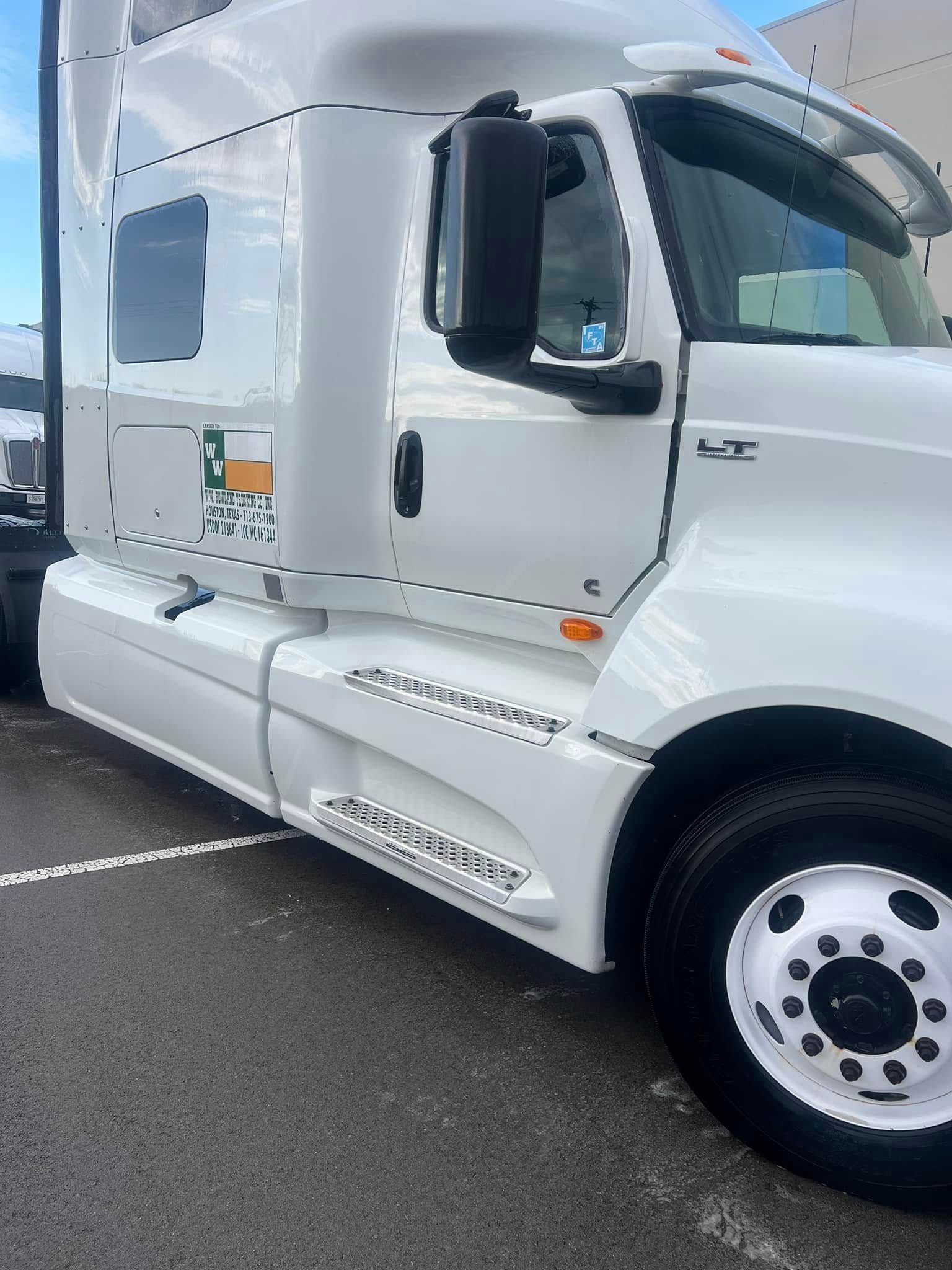 White semi-truck cab parked in a lot, side view with chrome details and tinted windows.
