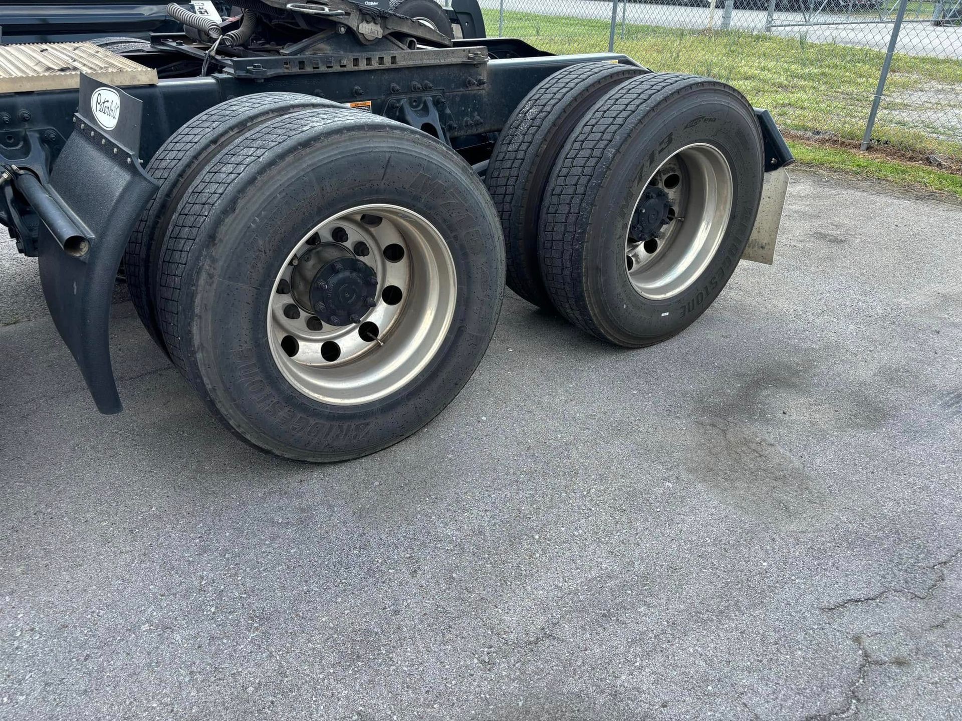 Close-up of dual truck rear wheels and tires on a paved lot near a chain-link fence.