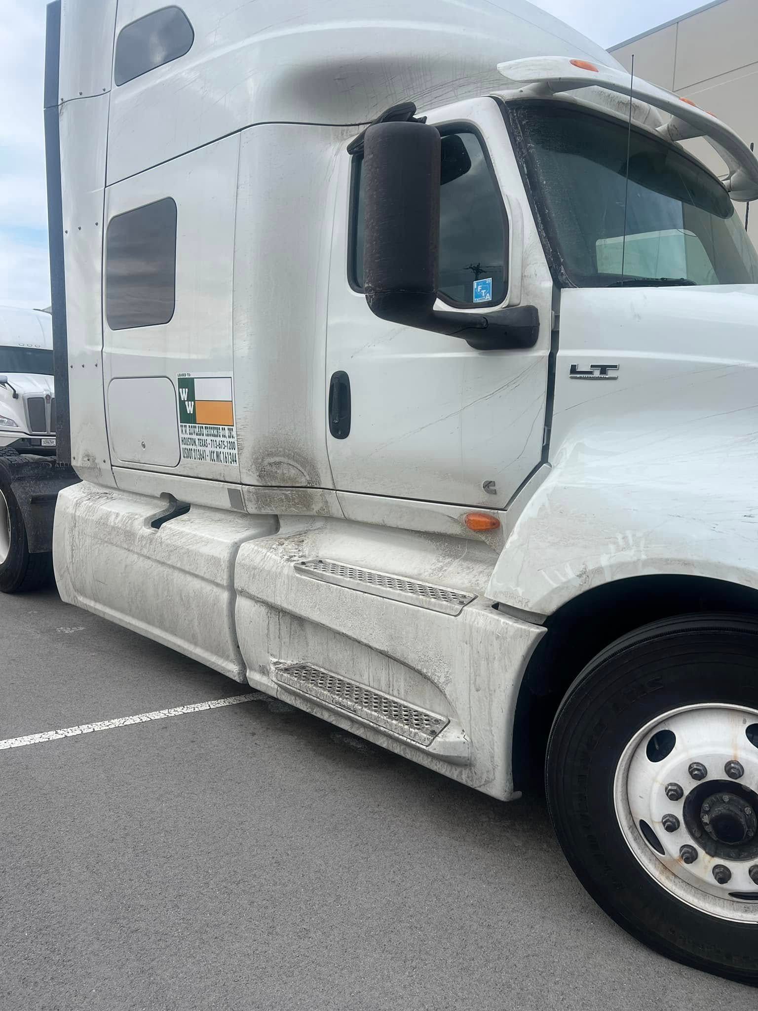 White semi-truck cab parked on a road, side view with silver fuel tank and black mirrors.