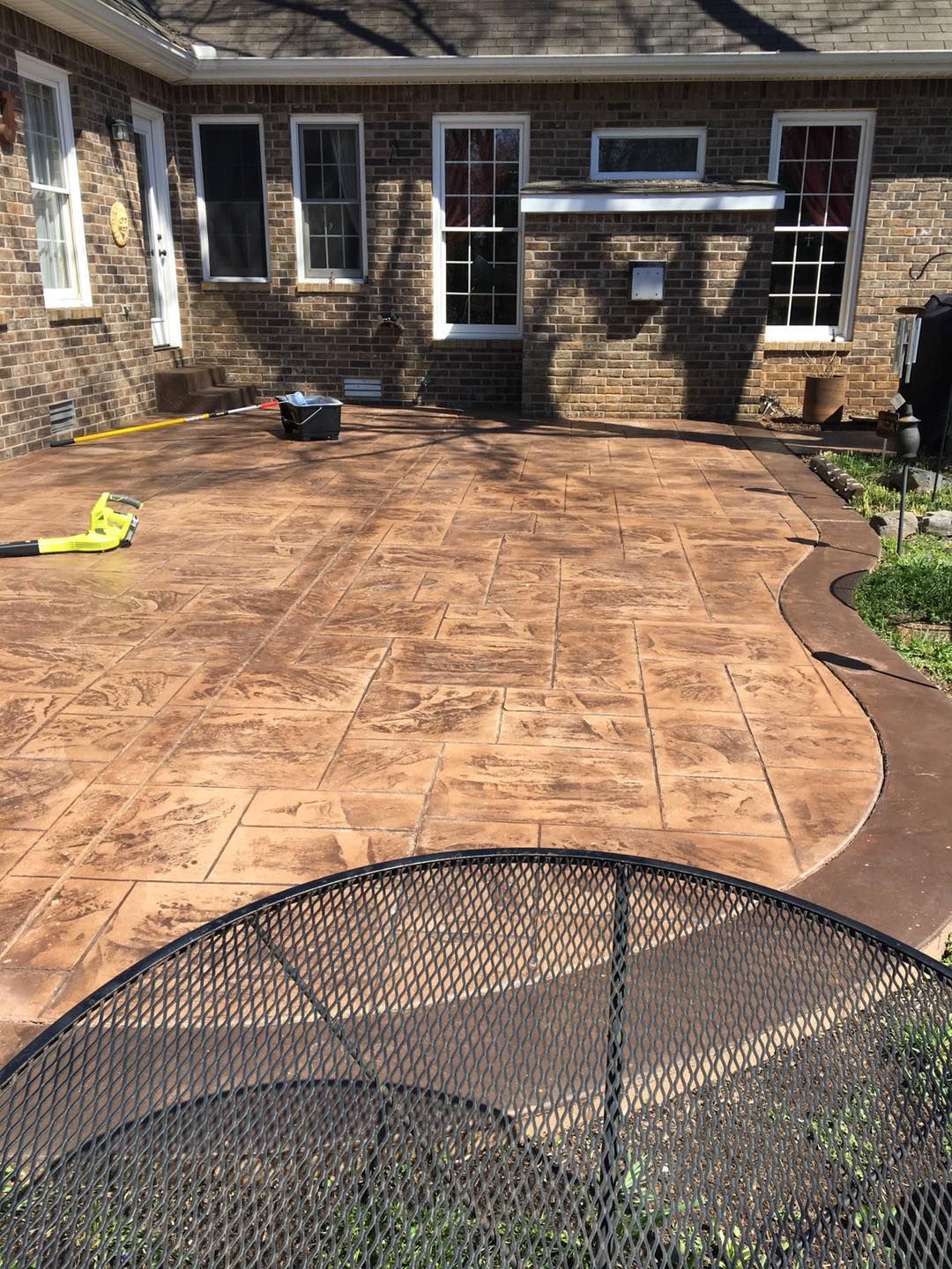 Patio with stamped concrete near a brick house, with a hose and a small black chair in the foreground.