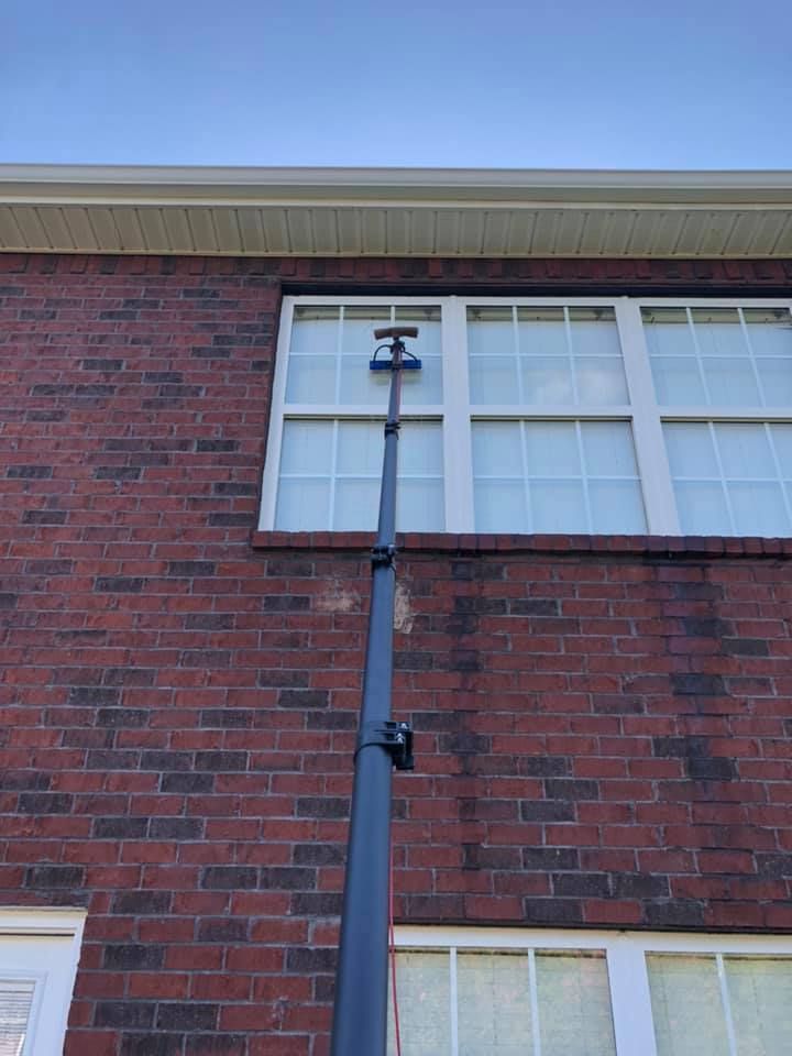 Brick building wall with a black downspout and two exterior lights beside a window.