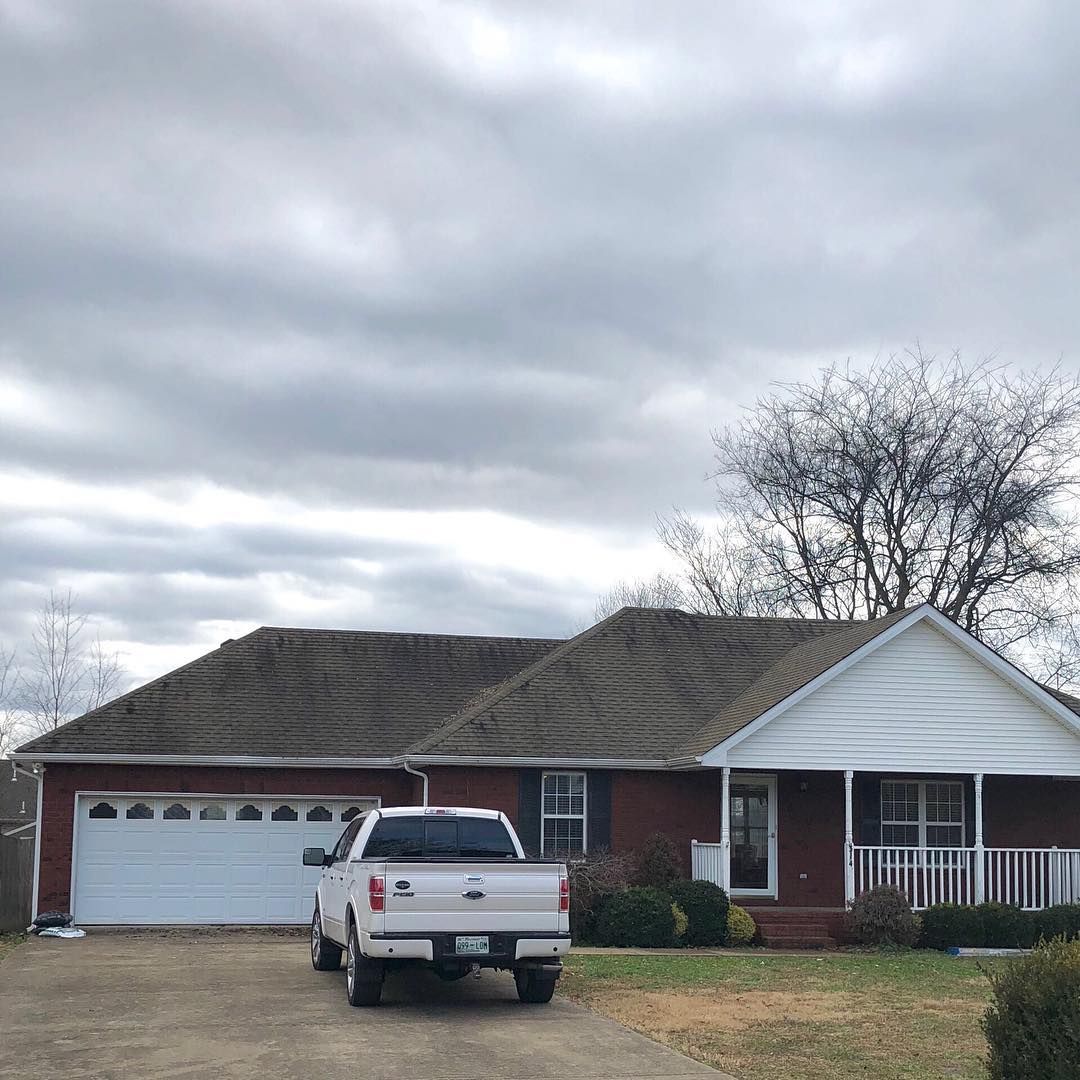 Suburban brick house with white garage and porch, white pickup truck parked in front under cloudy sky