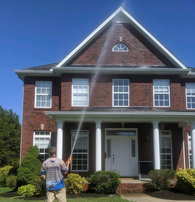 Person standing in front of a red-brick house with white columns and a front porch