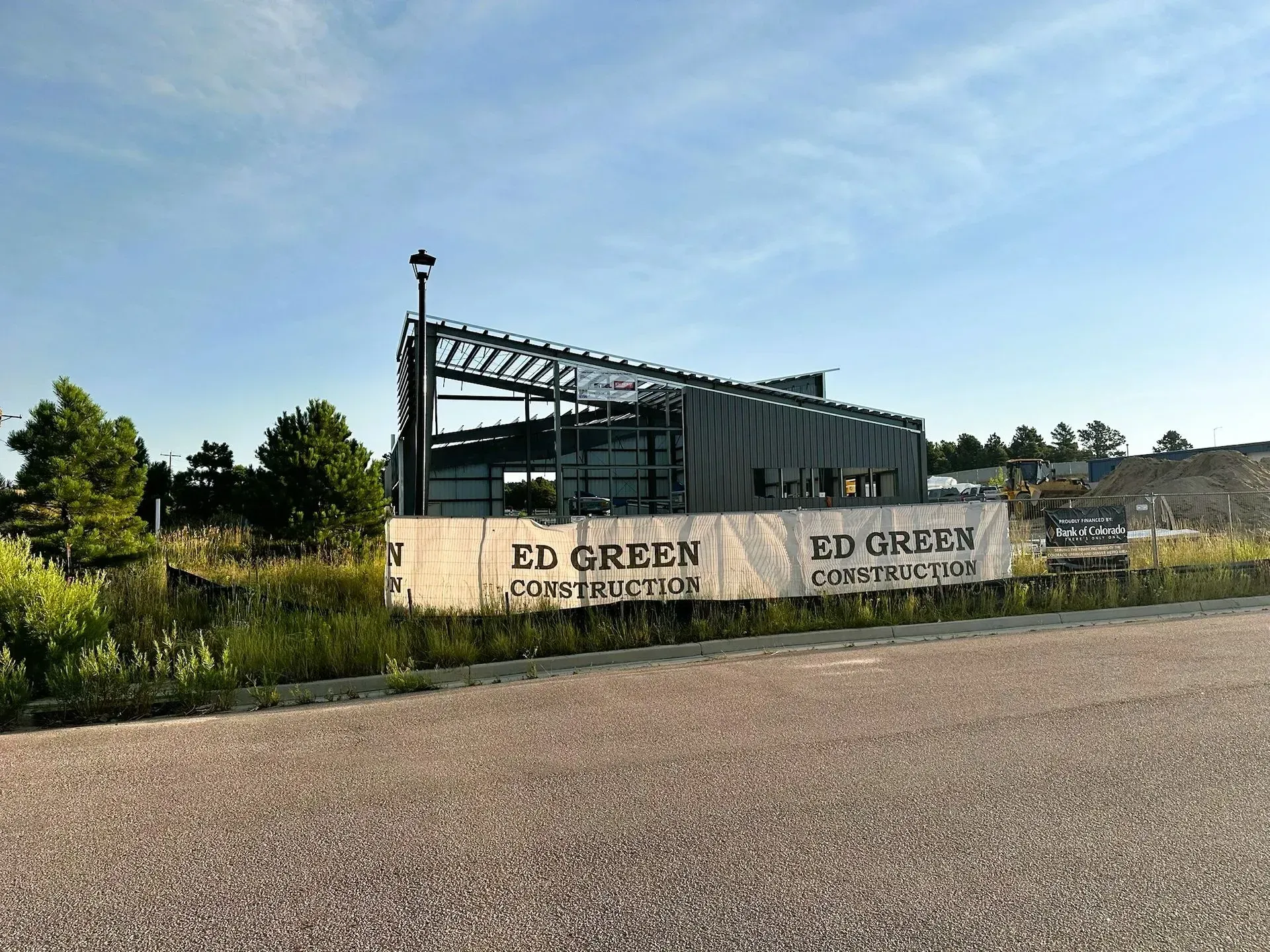 A partially constructed steel-frame building stands behind a white construction fence labeled Ed Green Construction.