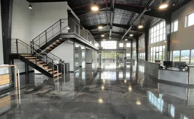 Spacious, modern industrial office interior with a mezzanine level, metal staircase, and polished gray epoxy flooring.
