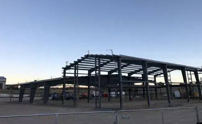 The grey steel skeletal frame of an industrial building under construction against a clear blue sky.